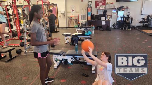 Two girls throwing a med ball to each other.