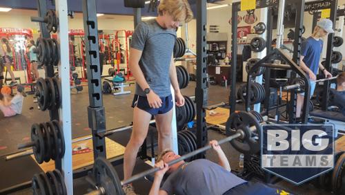 One boy bench pressing with another spotting the lifter.